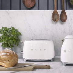 Smeg TSF01CREU Cream toaster styled on a marble kitchen counter next to matching kettle and fresh bread